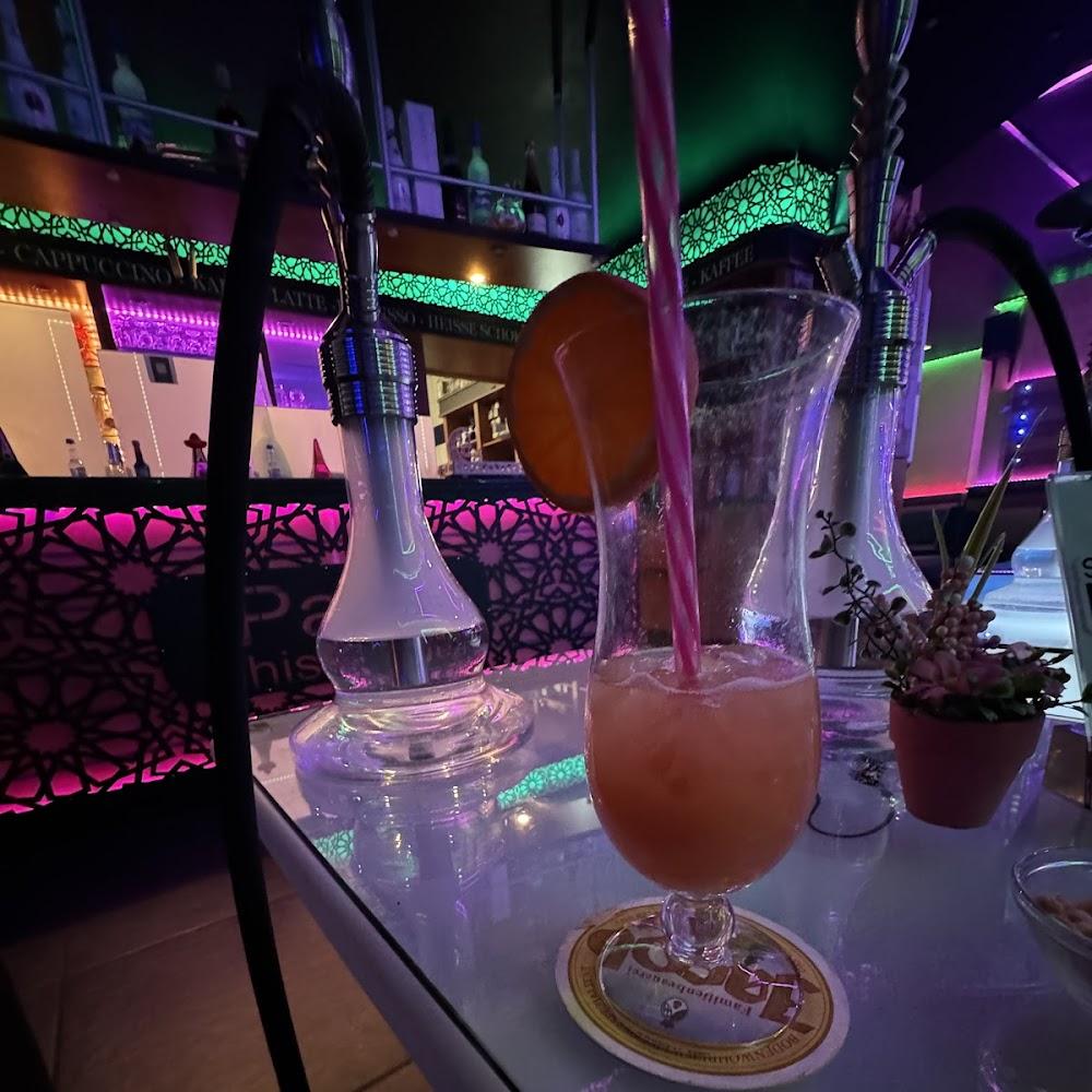 A pink drink with a straw in a glass, a hookah and a flower pot.